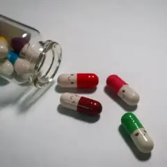 Kolorowe kapsułki, niektóre z uśmiechniętymi buźkami, wypadają z buteleczki. To mogą być psychotropy, które pomagają w trudnych chwilach.