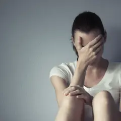 Kobieta siedzi przy ścianie, zakrywając twarz dłońmi. Czasem każdy potrzebuje chwili miansec, by zebrać myśli.
