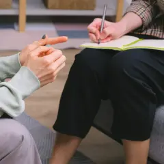 Dwie osoby rozmawiają o uzależnieniach behawioralnych. Jedna wskazuje palcem, druga notuje.