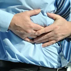 Mężczyzna w błękitnej koszuli i krawacie trzyma się za brzuch, odczuwając ból sugerujący powiększoną wątrobę.
