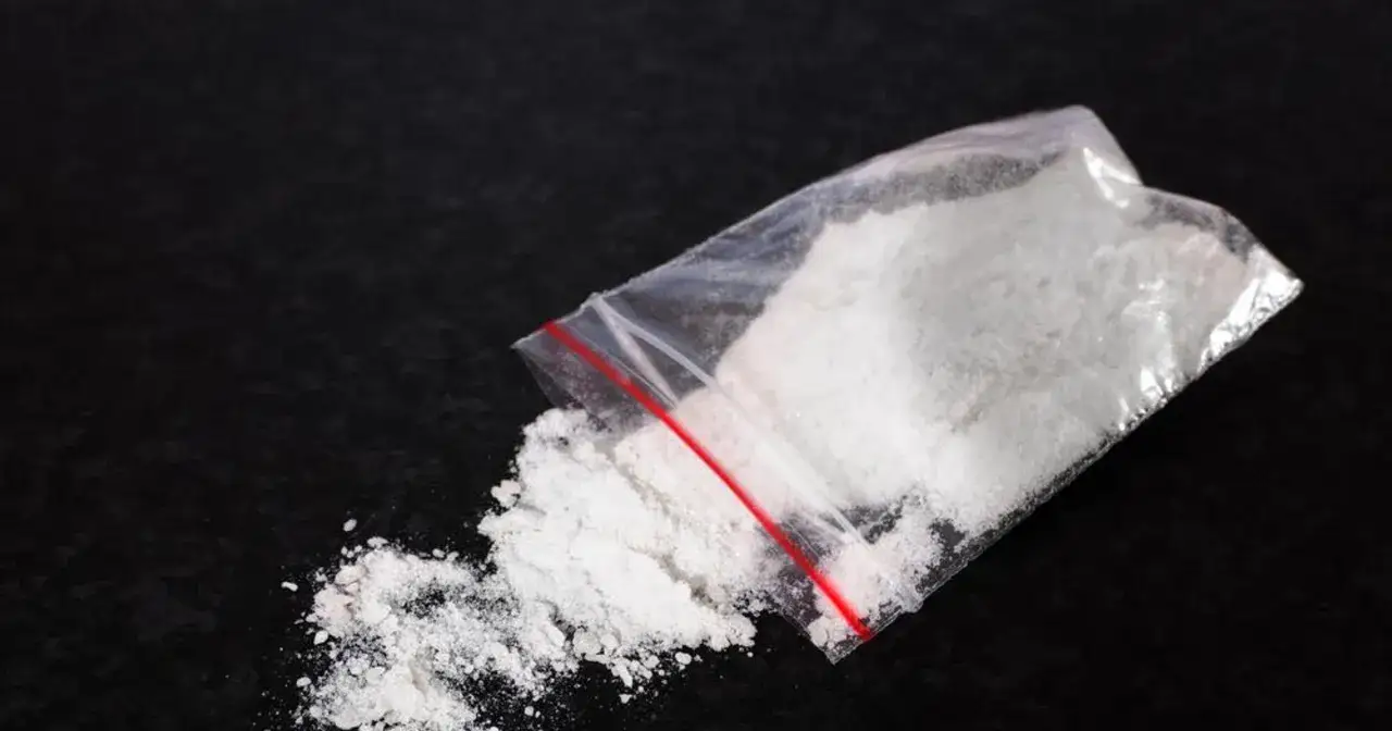 Biały proszek wysypujący się z plastikowej torebki z czerwonym zamknięciem. To może być mefedron, substancja psychoaktywna.