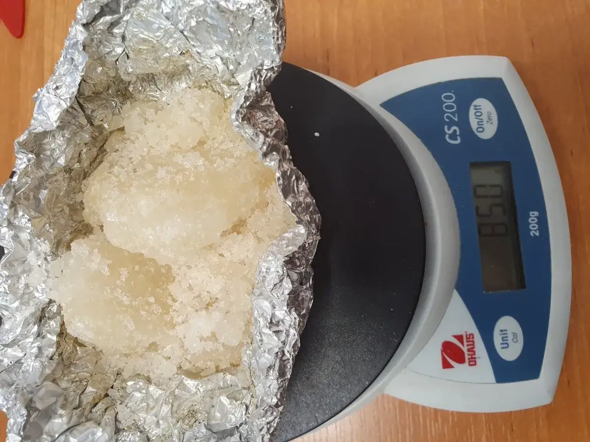 Biały proszek, prawdopodobnie klefedron, na wadze elektronicznej. Waga pokazuje 85.0 gramów.
