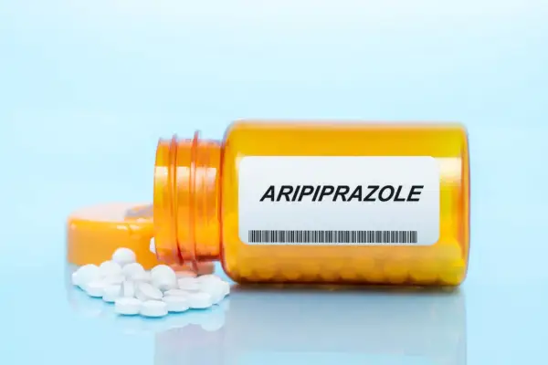 Pomarańczowa butelka z tabletkami, na etykiecie napis Aripiprazol. Kilka białych tabletek rozsypanych obok.